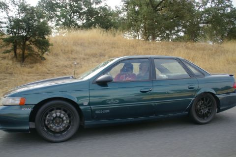 1995 Ford Taurus - Side view of a 1995 Ford Taurus sedan driving on a road.
