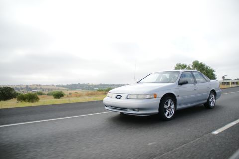 1995 Ford Taurus - Silver 1995 Ford Taurus sedan captured in a three-quarter front view while driving on a highway.