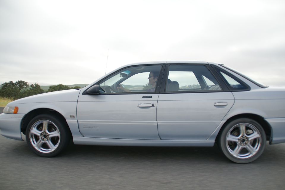 Silver 1995 Ford Taurus sedan driving on a road, side view