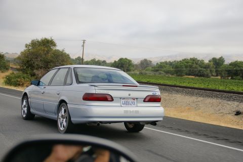 1995 Ford Taurus - A silver 1995 Ford Taurus SHO drives down a highway next to railroad tracks and a vineyard.