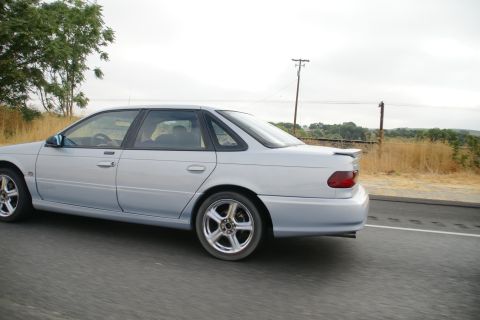 1995 Ford Taurus - Silver 1995 Ford Taurus sedan in motion on a highway with dry grass and trees in the background.
