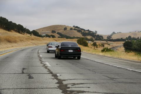 1995 Ford Taurus - A black 1995 Ford Taurus travels down a highway on a cloudy day, with another car ahead.