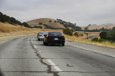 1995 Ford Taurus - Cars on a highway with rolling hills under a cloudy sky.
