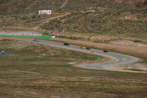 1995 Ford Taurus - Multiple vehicles navigate a challenging race track under a clear sky, with a prominent advertising sign visible on the distant hill.