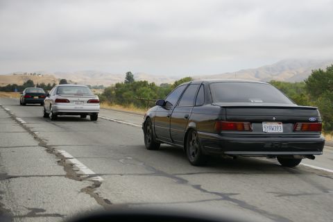 1995 Ford Taurus - A black 1995 Ford Taurus sedan is seen driving on a highway, with two other vehicles ahead.