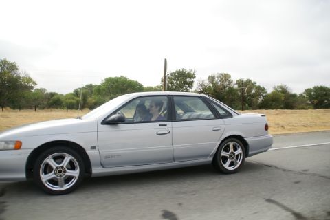 1995 Ford Taurus - A silver sedan is captured from the side as it travels down a highway.