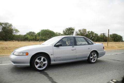 1995 Ford Taurus - A silver 1995 Ford Taurus sedan is seen from the side while driving on a road.