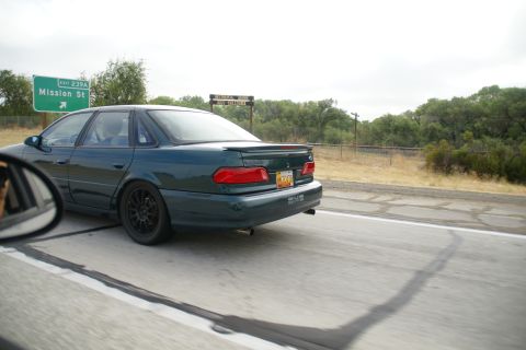 1995 Ford Taurus - A 1995 Ford Taurus sedan drives on a highway, with a "Mission St" exit sign visible.