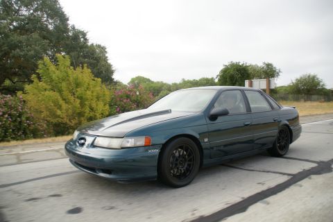 1995 Ford Taurus - 1995 Ford Taurus with aftermarket hood scoop and black wheels seen from the front-right.
