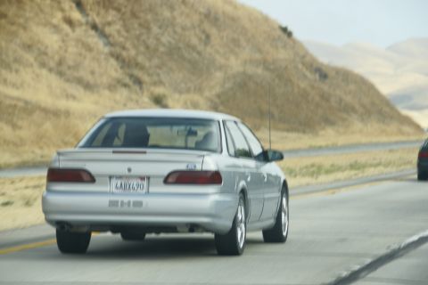 1995 Ford Taurus - Silver 1995 Ford Taurus sedan seen from behind on a highway with dry hills in the background.