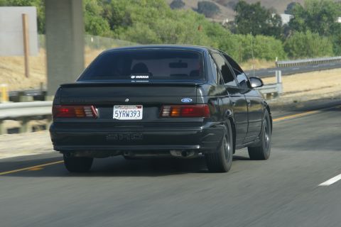 1995 Ford Taurus - This black sedan is seen from the rear while driving on a highway.