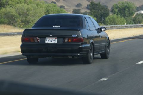1995 Ford Taurus - Rear view of a black 1995 Ford Taurus sedan on a highway.
