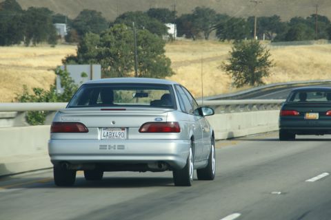 1995 Ford Taurus - A silver 1995 Ford Taurus sedan is seen from behind while driving on a highway, with another car in the adjacent lane.