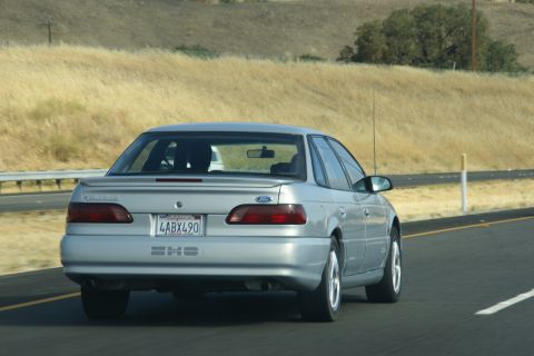 1995 Ford Taurus - Rear view of a silver 1995 Ford Taurus SHO driving on a highway with dry grass on the side.