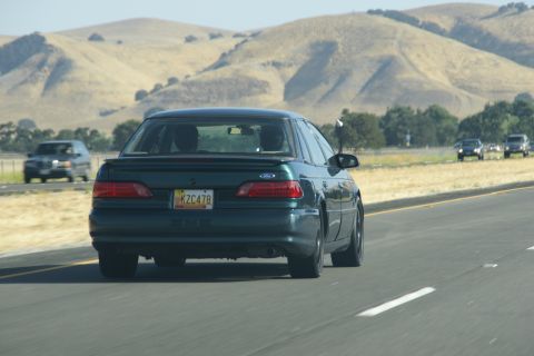 1995 Ford Taurus - A 1995 Ford Taurus is seen from the rear on a highway with rolling hills in the background.