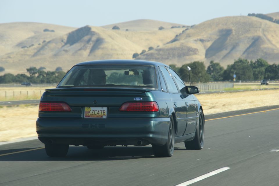 1995 Ford Taurus rear view driving on highway with hills in background