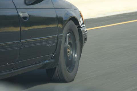 1995 Ford Taurus - A black car is captured in motion on a highway, focusing on its front wheel and side panel.