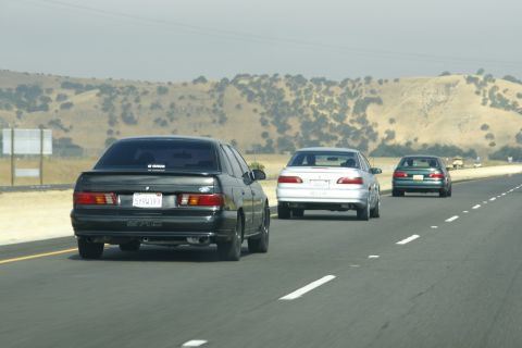 1995 Ford Taurus - Three cars travel down a highway with rolling hills in the background.