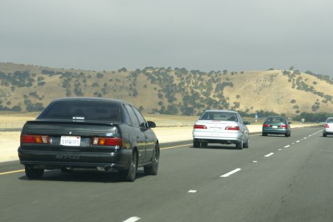 1995 Ford Taurus - A black Ford Taurus with a spoiler drives on a highway, with other vehicles ahead.