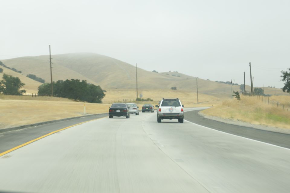 Multiple vehicles driving on a highway with rolling hills in the background