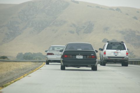 1995 Ford Taurus - Rear view of a black sedan on a highway, with a white SUV and a silver sedan also on the road.