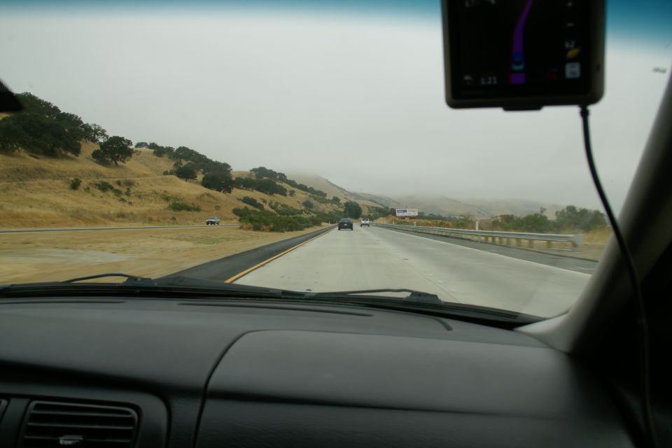 Dashboard view from inside a car on a highway with rolling hills and fog in the distance