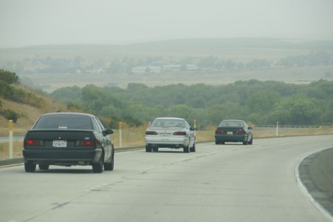 1995 Ford Taurus - Three cars drive on a highway with rolling hills and trees in the background.