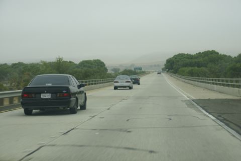 1995 Ford Taurus - A black 1995 Ford Taurus travels down a highway with other vehicles in the distance.