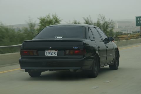 1995 Ford Taurus - Rear view of a black 1995 Ford Taurus sedan driving on a highway.