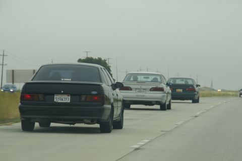 1995 Ford Taurus - Three sedans drive down a highway under an overcast sky.