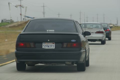 1995 Ford Taurus - Rear view of a black 1995 Ford Taurus on a highway, with other vehicles visible.