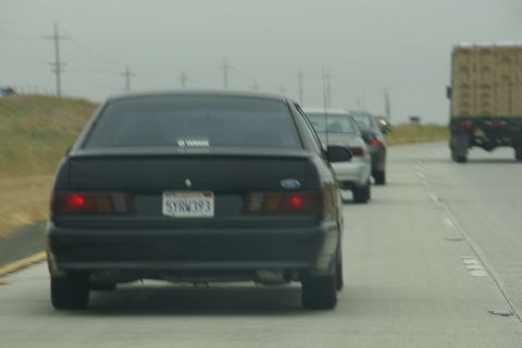 1995 Ford Taurus - A line of vehicles travels down a highway under an overcast sky.
