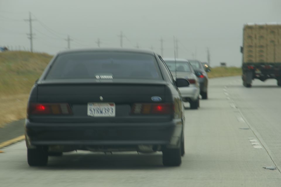 Rear view of a black sedan driving on a highway, with other cars and a truck ahead