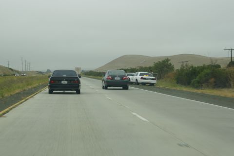 1995 Ford Taurus - A black sedan drives on a highway with other vehicles nearby under an overcast sky.