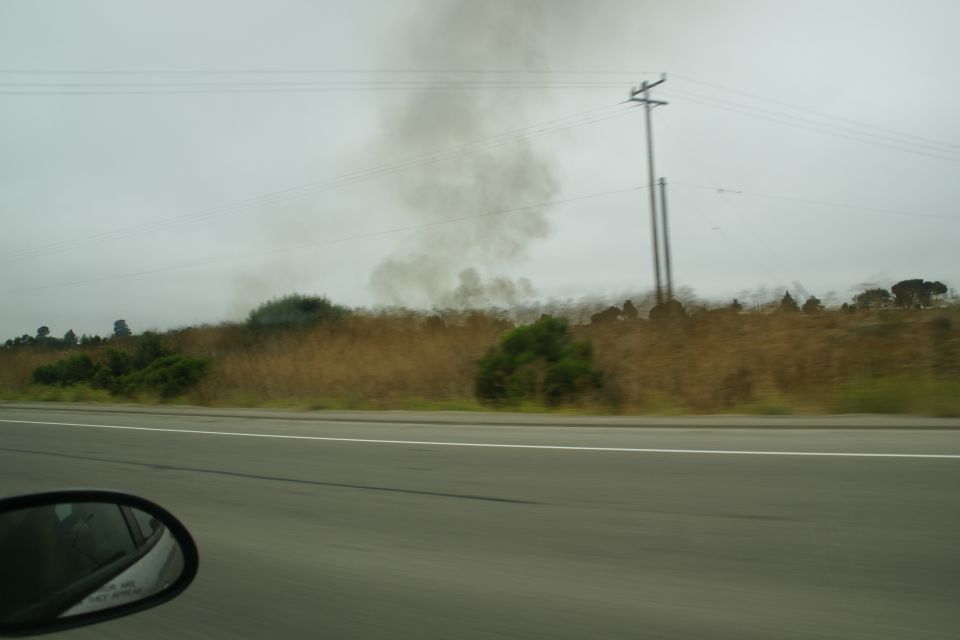 Smoke rising from a field next to a highway, with a utility pole in the background