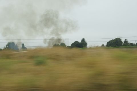 1995 Ford Taurus - Dark smoke rises from vegetation in a field, obscuring the horizon.