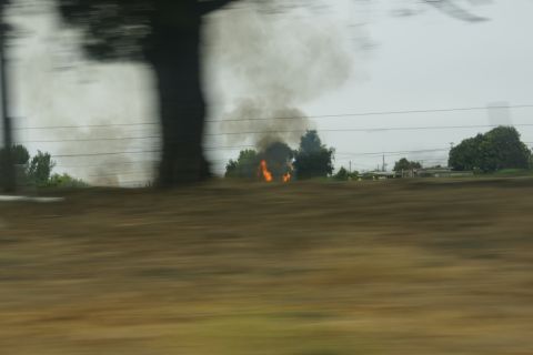 1995 Ford Taurus - A fire burns in a field, producing a large plume of smoke against an overcast sky.