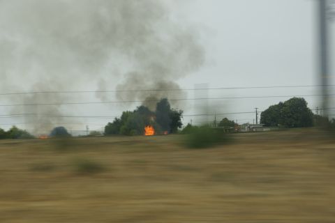 1995 Ford Taurus - A brush fire burns intensely amidst trees, sending thick plumes of dark smoke into the overcast sky.