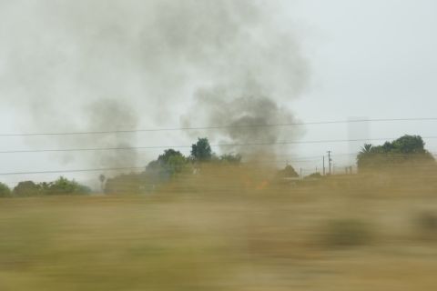 1995 Ford Taurus - A field is engulfed in smoke, obscuring the background with trees and utility poles visible through the haze.