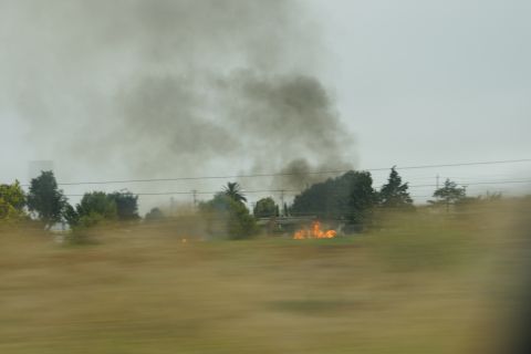 1995 Ford Taurus - A field fire sends dark smoke into the overcast sky, with flames visible near trees.