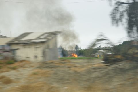 1995 Ford Taurus - A fire burns with smoke rising from a building and flames visible in a field, suggesting an emergency situation.