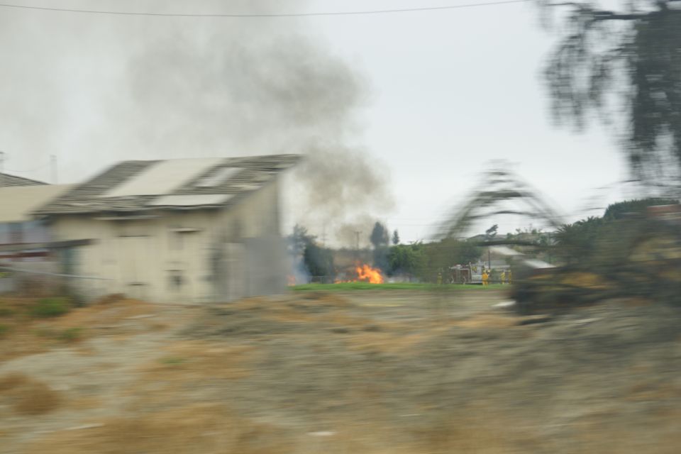Scene of a fire with smoke billowing from a building and flames in a field