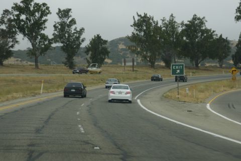 1995 Ford Taurus - Multiple vehicles travel on a highway under an overcast sky, with an exit sign visible.