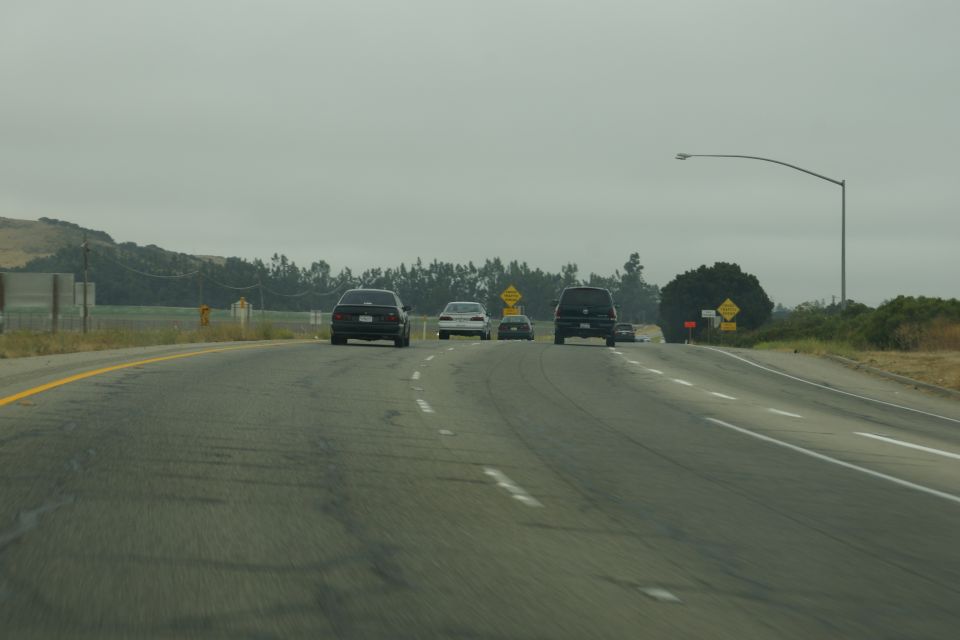 Several cars driving on a highway under an overcast sky
