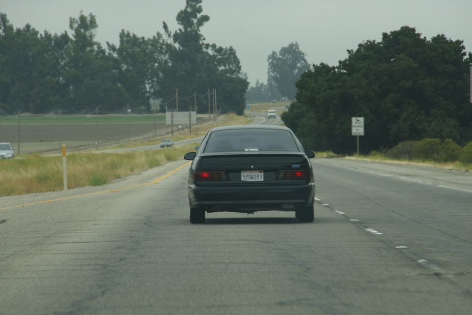 Rear view of a black 1995 Ford Taurus driving on a highway