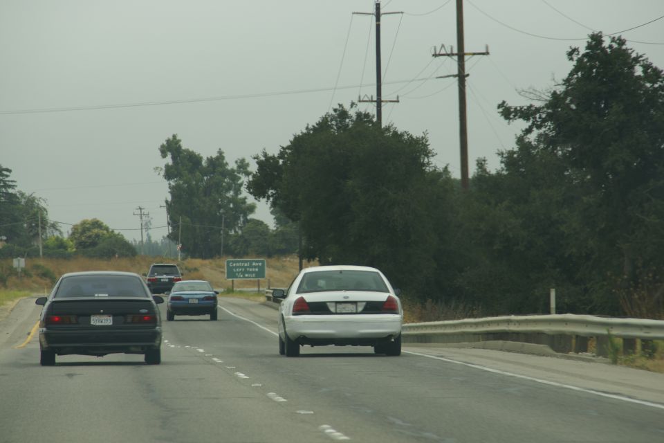 White Ford Crown Victoria from rear, driving on highway. License plate visible