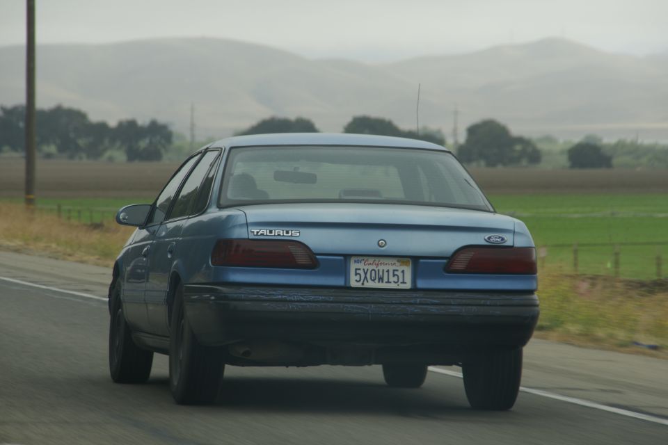 Blue 1995 Ford Taurus sedan driving on a highway, rear view. California license plate 5XQW151