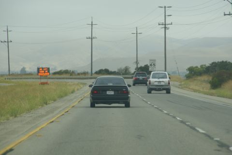 1995 Ford Taurus - A black sedan drives down a highway with a speed limit of 65 mph, under an overcast sky.