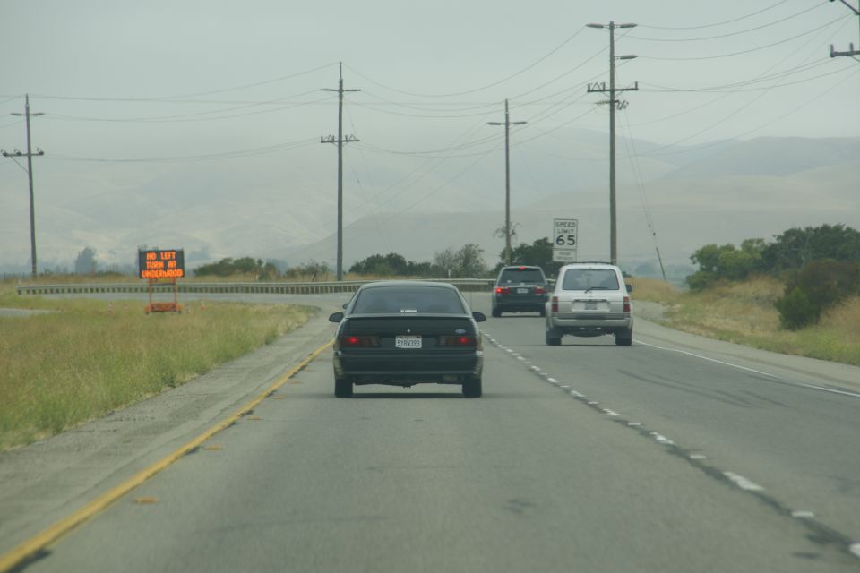 black sedan driving on highway, speed limit 65 sign, other cars ahead