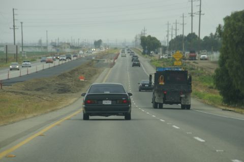 1995 Ford Taurus - A black 1995 Ford Taurus drives on a highway with construction ahead.